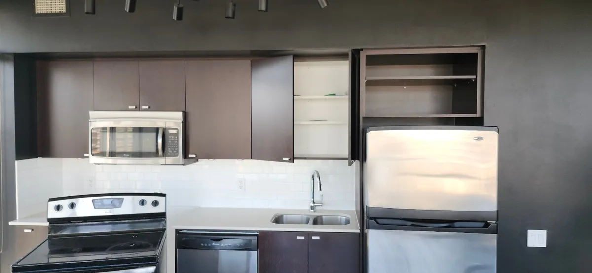 Empty condo kitchen before a move-in clean in Toronto, with cabinet doors open and the old fridge, range and dishwasher still in place